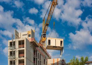 Grua levantando um módulo de madeira para cima de um prédio ainda em construção.