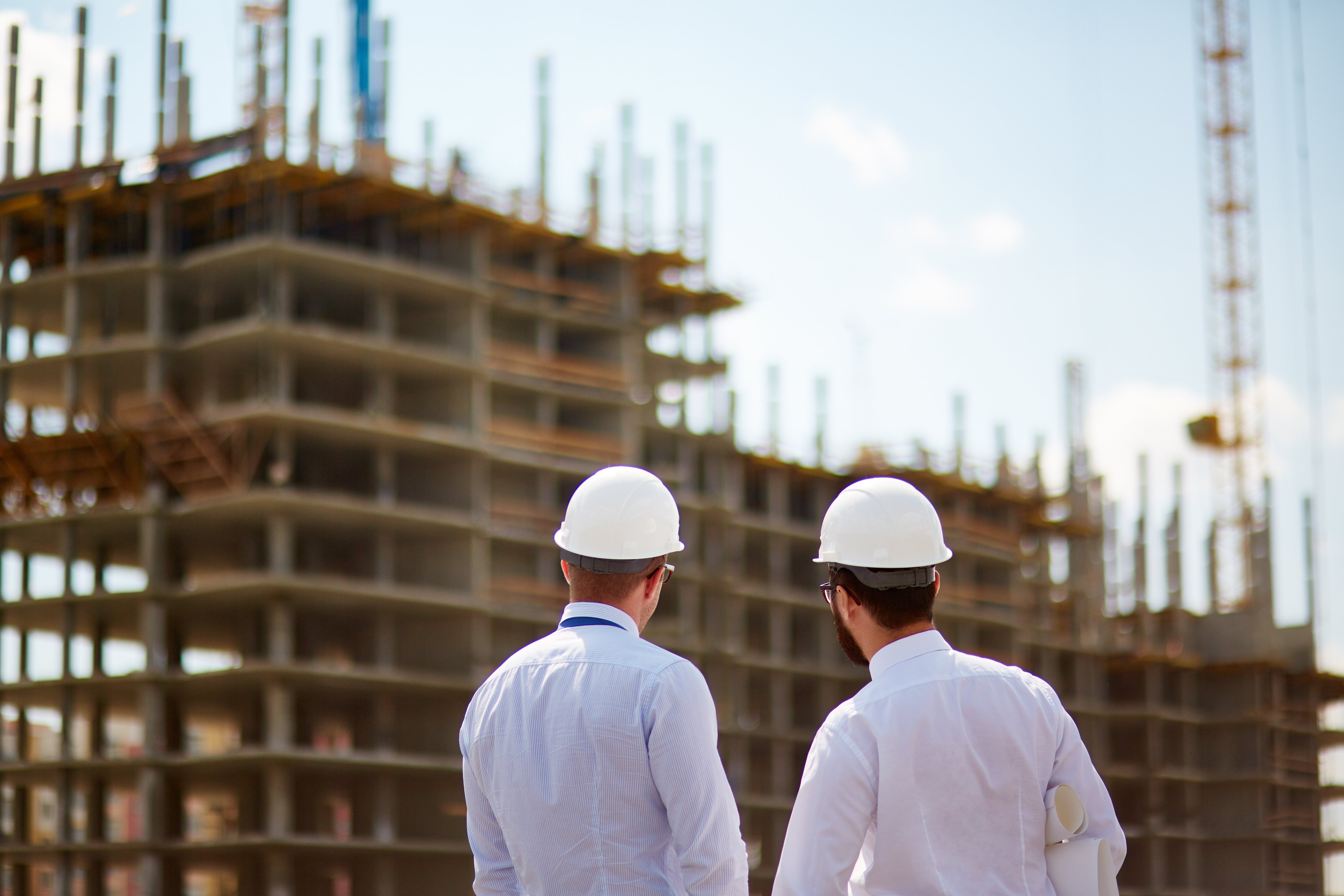 Dois engenheiros com imagem nítida olhando para o fundo um pouco borrado de um prédio em construção feito pela metade