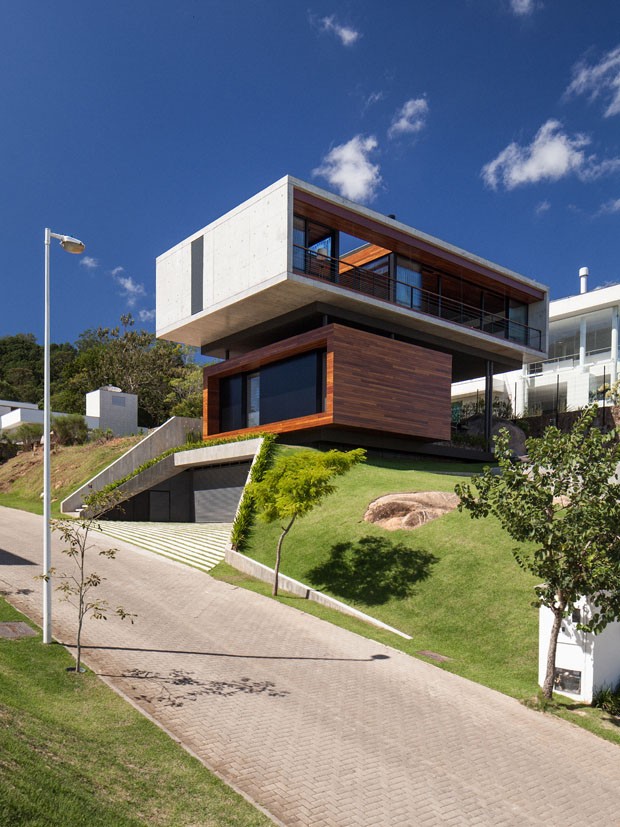 casa com construção suspensa com destaque para a sacada detalhamento em vidro e madeira e jardim ao redor