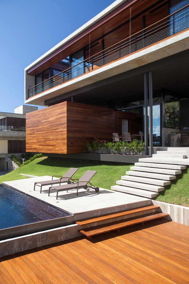 casa com construção suspensa detalhes e madeira e com piscina e arvores ao redor