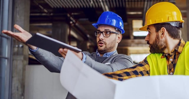 Foto de dois homens em uma construção, ambos parecem estar discutindo sobre trabalho, com foco em algum aspecto do projeto