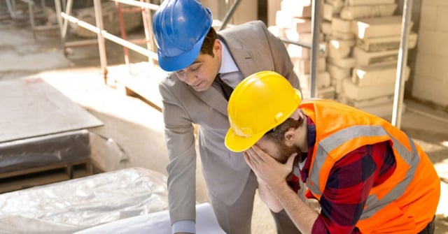 Dois homens em um canteiro de obras. Um deles, parece estar sob stress, o outro parece estar falando com o colega preocupado
