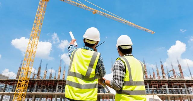 Engenheiro discutindo obra com mestre de obras e guindaste trabalhando ao fundo